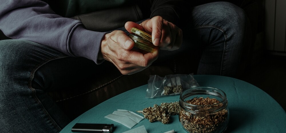 man grinding weed into a jar that will hold a quarter of weed