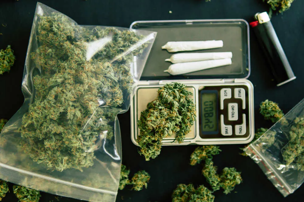 an ounce of weed in a bag with two joints on a weighing scale next to it